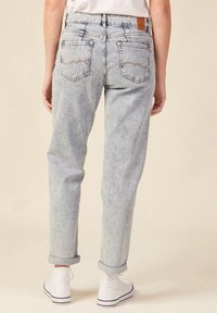 Jeans de mezclilla azul claro con un corte relajado, dobladillos enrollados y dos bolsillos traseros con costuras curvadas. Combinados con zapatillas blancas.