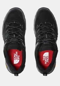Chaussures de randonnée noires avec crochets de laçage, en tissu en maille, et semelles intérieures rouges arborant le logo The North Face.