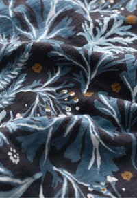 Tessuto di cotone con uno sfondo blu scuro e intricati motivi di foglie blu, accentuato da dettagli floreali gialli e bianchi.