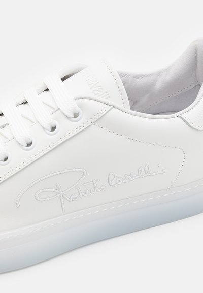 Zapatilla blanca de cuero con cuello acolchado, cordones blancos y detalle característico en el costado. Suela de goma translúcida con acentos cosidos.