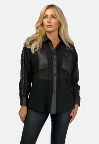 Czarna półprzezroczysta koszula z skórzanymi akcentami, dwoma przednimi kieszeniami i ćwiekowanymi detalami na rękawach, z zapięciem na guziki i kołnierzykiem.