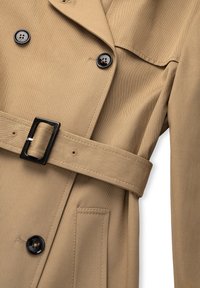 Tan trench coat with black buttons, a matching fabric belt with a black rectangular buckle, and a front pocket on the right side.
