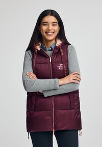 Bordeauxfarbene Steppweste mit Kapuze, ausgestattet mit einem glänzenden roségoldenen Futter, Reißverschluss und "Polo Club"-Branding an den Trägern und auf der Brust.