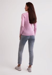 Ljusrosa långärmad tröja i kombination med ljusa jeans. Jeansen är uppvikta vid fållarna, och outfiten fulländas med ljusa sneakers.