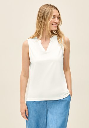 Haut sans manches blanc avec un design en V, en tissu doux et coupe décontractée. Porté avec un pantalon bleu clair ample.