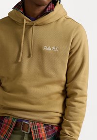 Felpa con cappuccio in una tonalità marrone dorato con tessuto testurizzato. Presenta il logo "Polo R.L." ricamato e il colletto a quadri sovrapposto visibile.