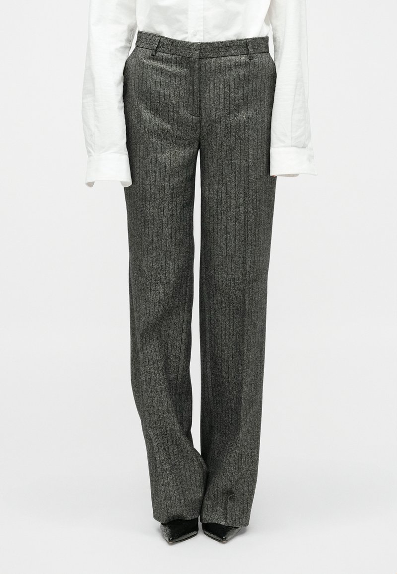 Sive prugaste hlače s krojenim fitom, ravnim prednjim dijelom, bočnim džepovima i ravnim dizajnom nogavica. Tkanina pokazuje suptilnu teksturu i sjaj.