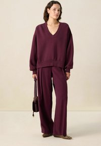 Sweatshirt bordeaux à col en V avec épaules tombantes et ourlet côtelé, associé à un pantalon bordeaux ample. Chaussures à imprimé serpent.