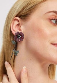 Punased ja mustad lillede kõrvarõngad roheliste lehe aktsentidega, millel on metallist hõbedane varrekujundus. Nähtavad tekstureeritud pind ja sädelevad detailsed elemendid.