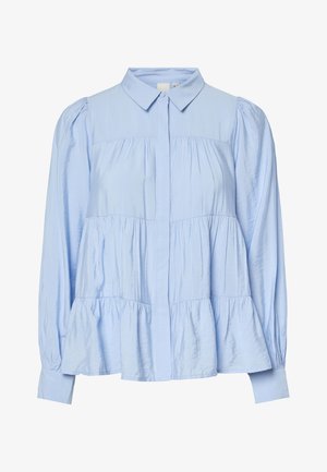 Blouse bleu clair à manches longues avec volants superposés, boutonnée sur le devant, col pointu et détails froncés sur les manches et le corps.
