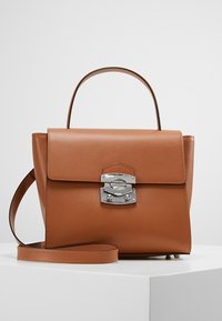 Sac à main en cuir marron avec une forme structurée, fermeture en métal argenté et une bandoulière amovible. Texture lisse et design minimaliste.