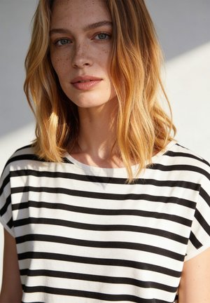 Jonge vrouw met schouderlang blond haar en sproeten, gekleed in een zwart-wit horizontaal gestreept shirt, kijkt iets naar links.