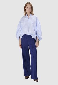 Chemise oversize à rayures bleu clair avec boutonnage sur le devant, associée à un pantalon large bleu marine et des talons à imprimé animalier. Accessoires simples inclus.