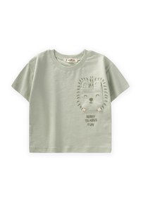 Camiseta de algodón verde claro con mangas cortas, que presenta un bolsillo bordado con la cara de un león y el texto "LISTO PARA DIVERTIRSE" debajo.