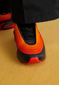 Nike sportcipő narancs és piros színátmenetes anyaggal, fekete részletekkel és textúrált gumitalppal. Látványos fűzők és logó részlet.