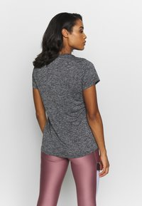 Camiseta gris de manga corta con una textura suave, diseño ajustado y escote redondeado, combinada con leggings rosas. Vista trasera mostrada.