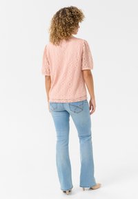 Pink lace top with a textured diamond pattern, puffed short sleeves, and a relaxed fit. Paired with light blue flared jeans.