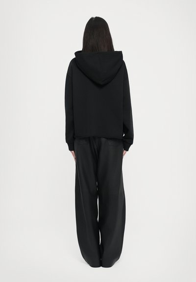 Svart kort hoodie med huva och långa ärmar, kombinerad med lösa svarta byxor. Mjuk textur, minimalistisk design utan synliga mönster.