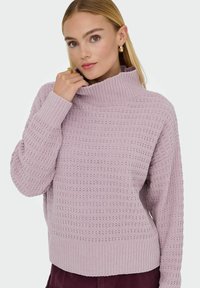 Pull en tricot lavande clair avec un col haut, un motif texturé, une coupe ample et des poignets et un ourlet côtelés. Détails de motif subtils sur l'ensemble.