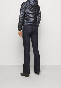 Kiiltävä musta toppatakki, jossa vaakasuorat tikkauskuviot, yhdistetty tummiin denim-leveälahkeisiin farkkuihin. Asun täydentävät nahkasaappaat.