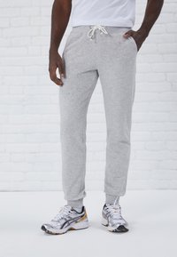 Pantalones de chándal grises con cintura ajustable, puños acanalados y bolsillos laterales. Combinados con zapatos deportivos plateados y negros. Diseño simple.