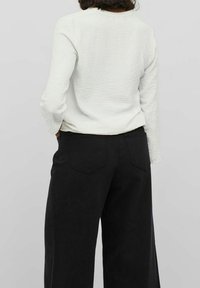Chemise blanche à manches longues avec texture, associée à un pantalon noir à jambes larges et taille haute, doté de deux poches arrière. Design minimaliste.