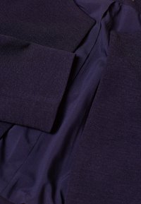 Blazer blu navy scuro con esterno testurizzato, fodera interna liscia e spalle strutturate, maniche aperte e taglio classico.