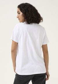 T-shirt blanc à manches courtes avec un col rond, en coton doux, coupe décontractée et texture lisse. La vue arrière montre la simplicité du design.