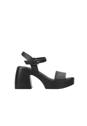 Sandalias negras de tacón alto con una plataforma gruesa, que presentan una amplia tira frontal y una tira de tobillo con un hebilla de metal. Acabado en cuero suave.