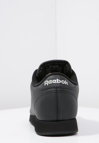 Basket noire Reebok avec une tige en cuir lisse, un col rembourré et un logo blanc sur l'arrière. Semelle extérieure en caoutchouc plate.