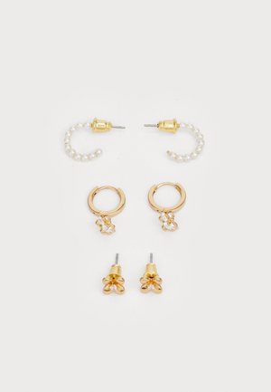 Quatre paires de boucles d'oreilles : créoles dorées avec des perles, créoles dorées avec des charms floraux, et boucles d'oreilles percées en forme de fleurs, toutes avec des finitions brillantes.