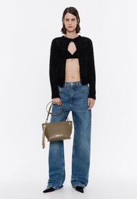 Black cropped fuzzy cardigan with keyhole cutout, high-waisted blue denim jeans, and a small olive green handbag with gold accents.