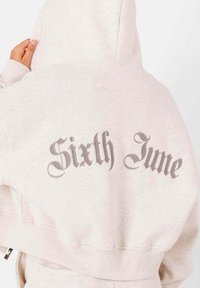 Ljust grå hoodie med en mjuk textur. Har ett stort, stiliserat "Sixth June" i mörkgrått på baksidan. Ribbad mudd på ärmar och nederkant.