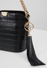 Borsa in pelle nera con motivo coccodrillo, dotata di dettagli in oro, inclusi una tracolla a catena e un accento a frange con un dettaglio circolare del logo MK.