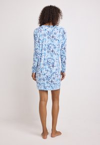 Abito a maniche lunghe di colore azzurro chiaro con motivi floreali in blu navy. Tessuto morbido, lunghezza al ginocchio, aderente in vita, con scollatura rotonda.