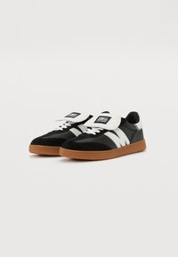 Schwarz-weiße Sneaker mit einem Obermaterial aus Wildleder und Synthetik, runder Zehenpartie, gepolsterter Zunge und Gummisohle mit kontrastierenden Streifen.