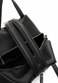 Mustast nahast käekott tekstuurse viimistlusega, millel on kaks tõmblukku, kuldse tooni metalldetailid ja kaks lühikest sangagi kandmiseks.