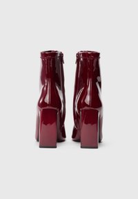 Botins de tornozelo em pele verniz bordeaux com um design elegante, saltos quadrados e fecho de correr na parte de trás para facilitar o calçar.