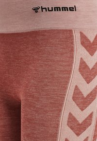 Hummel atletiska leggings i en urbleknad röd nyans, med en ribbad textur och ett kontrasterande ljusrosa zigzag-mönster längs sidan.