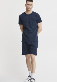Tricou croșetat scurt, de culoare bleumarin, cu un buzunar pe piept, asortat cu șorturi. Fabricat dintr-un material moale, având o croială lejeră și un design minimalist.
