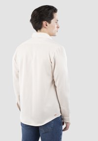 Lys beige skjorte med langeærmer, knapkrave og klassisk pasform. Har subtil tekstur og et lille logo fra mærket på kanten.