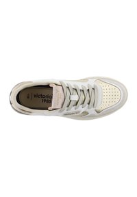 White sneaker with a perforated beige toe cap, gray laces, and metallic accents. Features a logo on the tongue and multiple texture details.