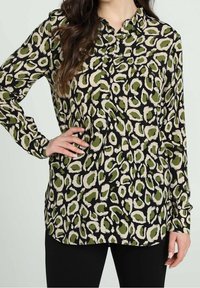 Camicia a maniche lunghe, sfondo nero con stampa animale verde e beige, colletto button-down, tessuto morbido, vestibilità leggermente ampia, orlo curvo.