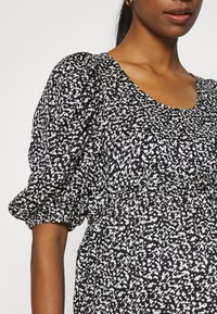 Vestido com padrão preto e branco, apresentando mangas bufantes, um decote redondo e uma cintura franzida. Tecido suave com uma textura leve.