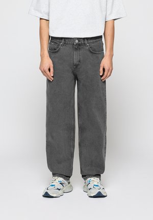 Jeans de mezclilla gris con un corte holgado, diseño de cinco bolsillos y cierre de botón. Combinados con una camiseta gris y zapatillas multicolores.