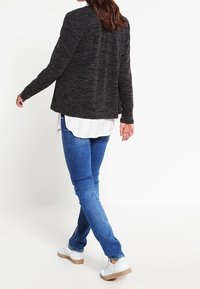 Ciemnoszary, teksturowany żakiet o luźnym kroju, noszony na białej koszuli, w zestawieniu z niebieskimi dżinsami i białymi trampkami.