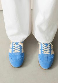 Blauwe suède en beige textielen sneakers met witte veters, voorzien van een gebogen ontwerp, geschulpte randen en een textuur rubberen zool.