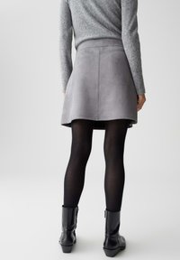 Gonna in suede grigia con orlo svasato, abbinata a collant neri e stivaletti neri. Maglione a maglia testurizzata visibile nella parte superiore.