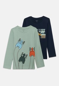 Zwei Langarm-T-Shirts: eines grün mit Traktor-Grafiken und Reifenspuren, das andere marineblau mit landwirtschaftlichem Text und Tiermuster.