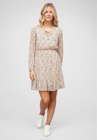 Robe à manches longues avec motif floral en tissu rose clair, taille froncée, ourlet à volants et détail d'encolure en forme de trou de serrure. Associée à des baskets blanches.